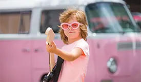 En ung kille som lirar elgitarr med rosa solglasögon och rosa tröja framför en rosa volkswagenbuss.